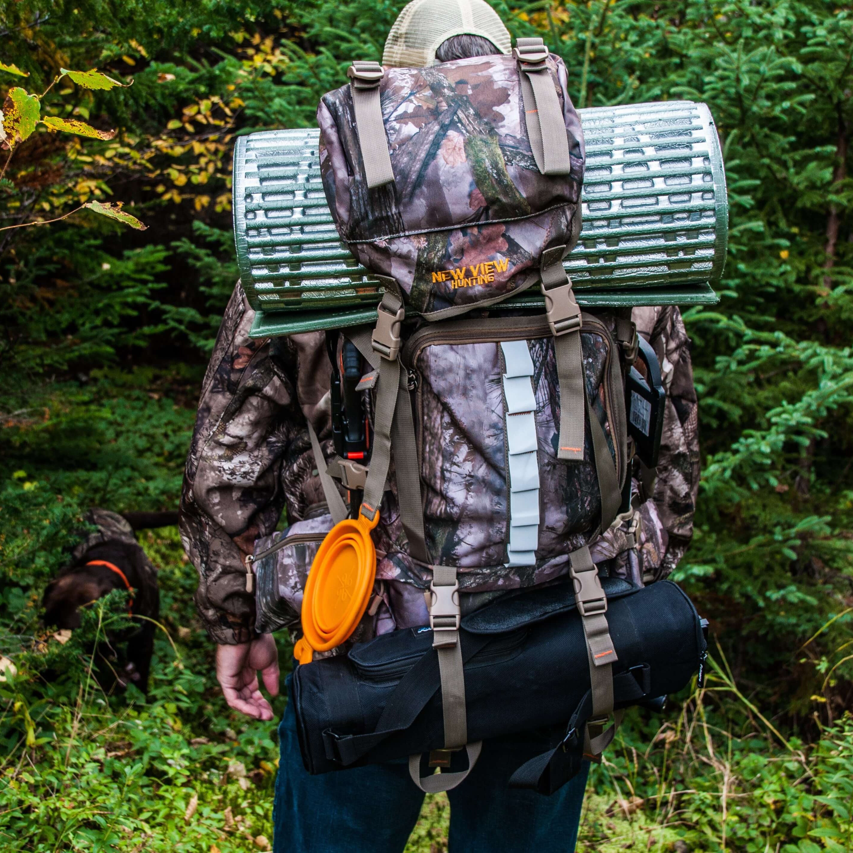 Hunter carrying a large camouflage hunting backpack with gear attached in woodland