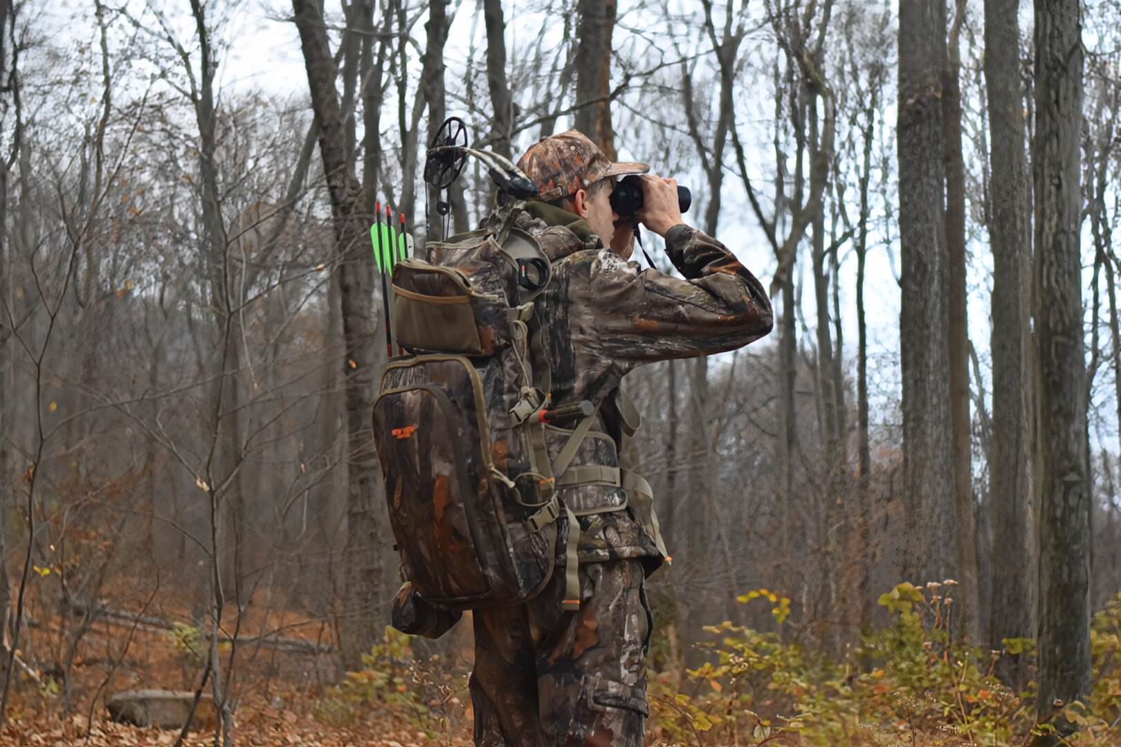 Hunter carrying a bow hunting pack with a compound bow and arrows in woodland