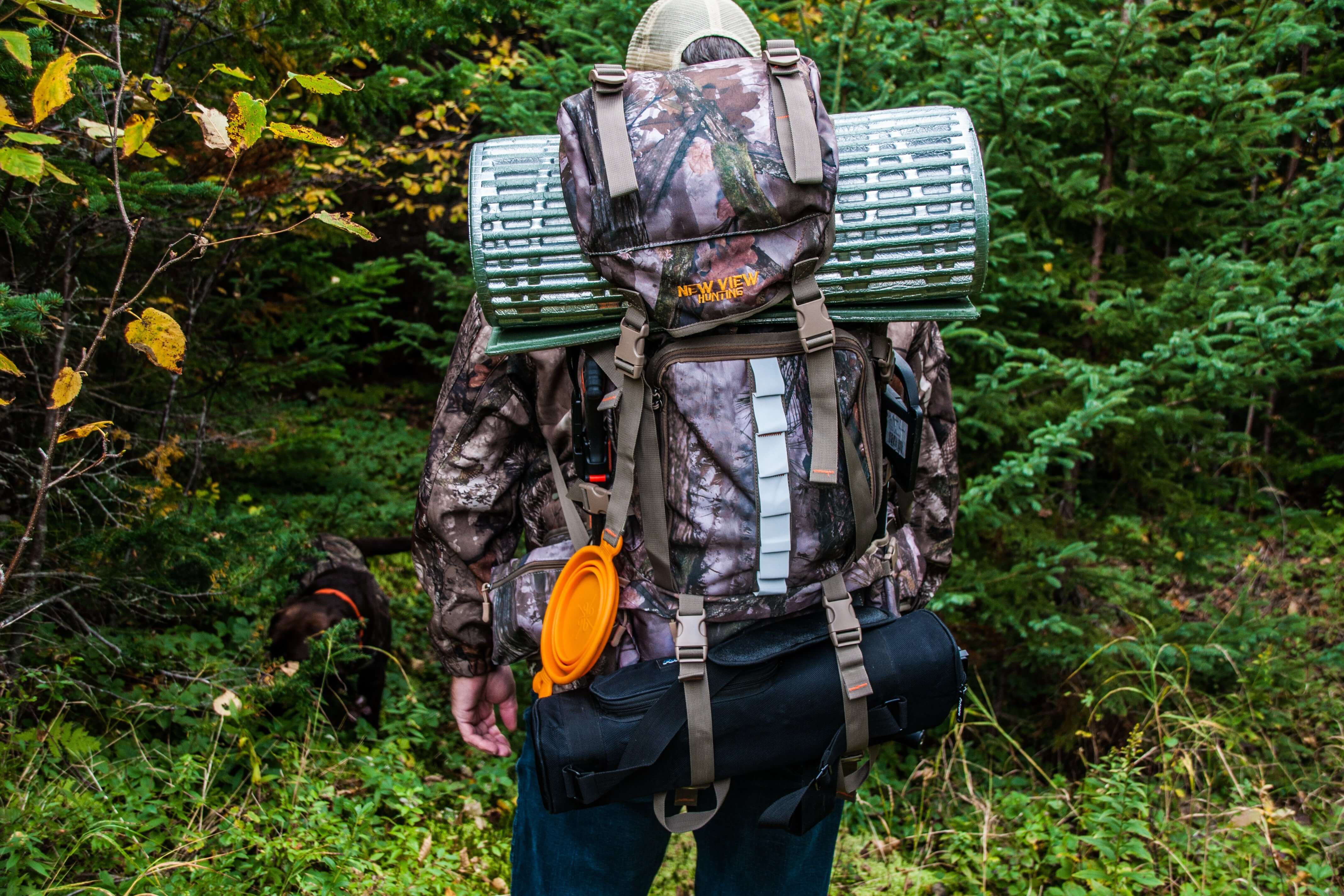 Hunter carrying a large camouflage hunting backpack with gear attached in woodland