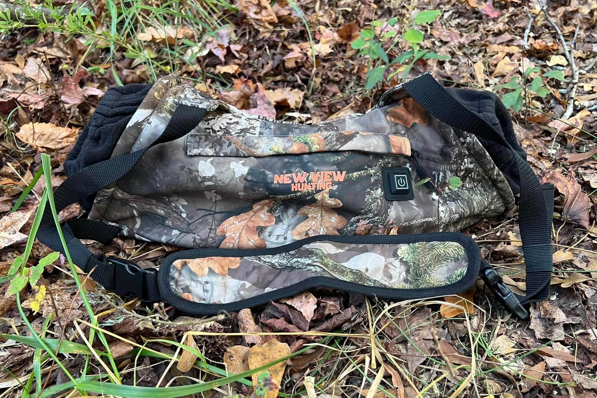 Heated camouflage hand muff and hunting gear on a woodland floor