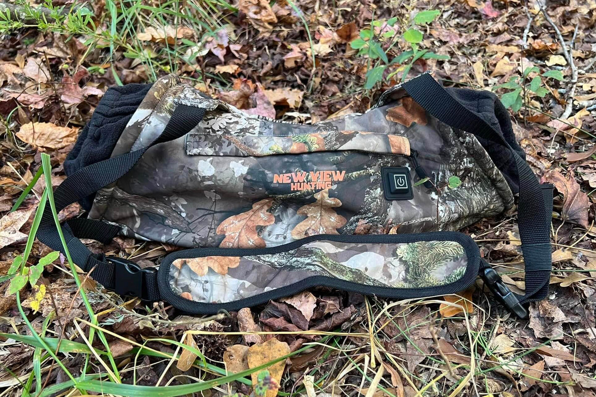 Heated camouflage hand muff and hunting gear on a woodland floor